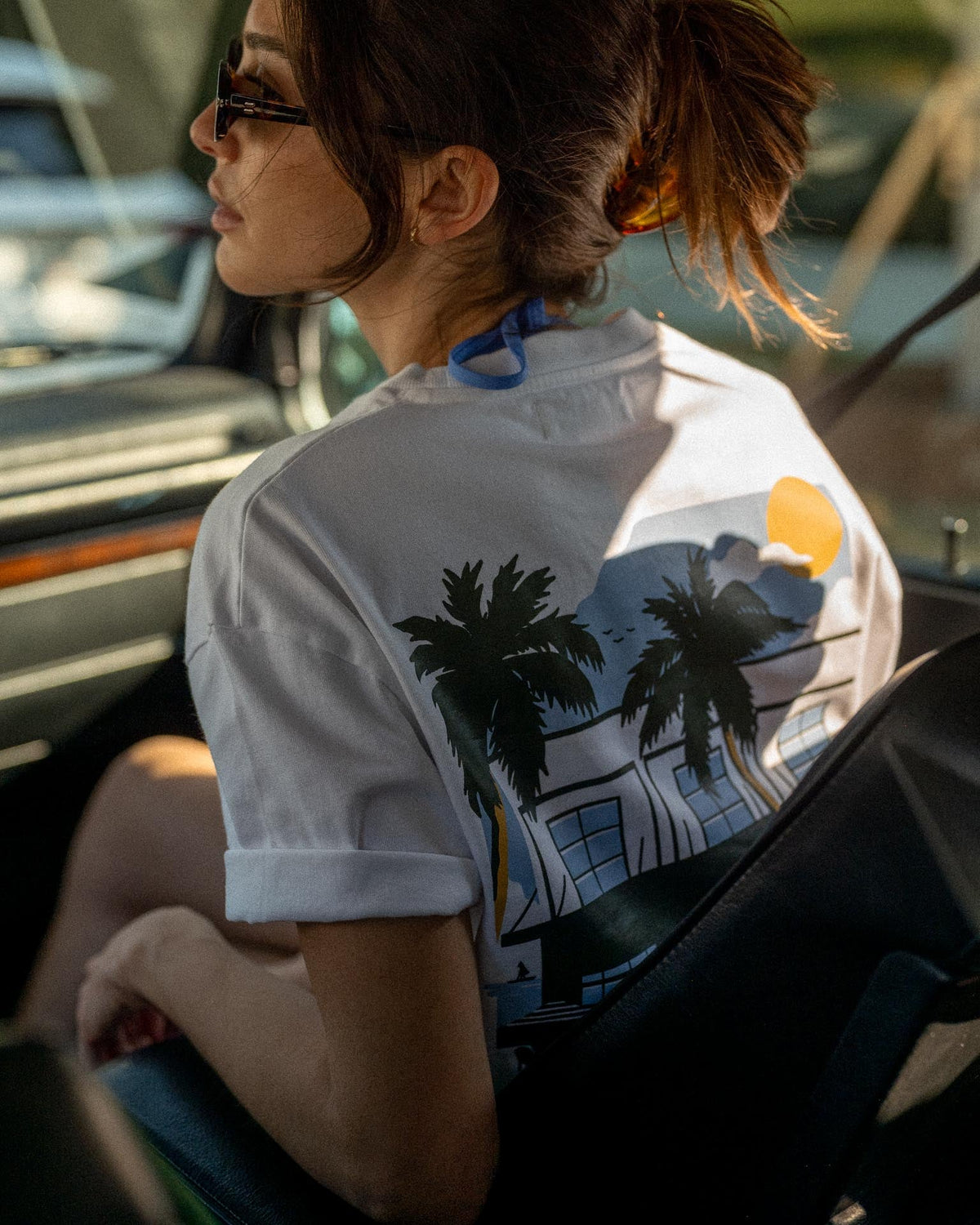Person wearing a white shirt with palm tree design sitting inside a vehicle.